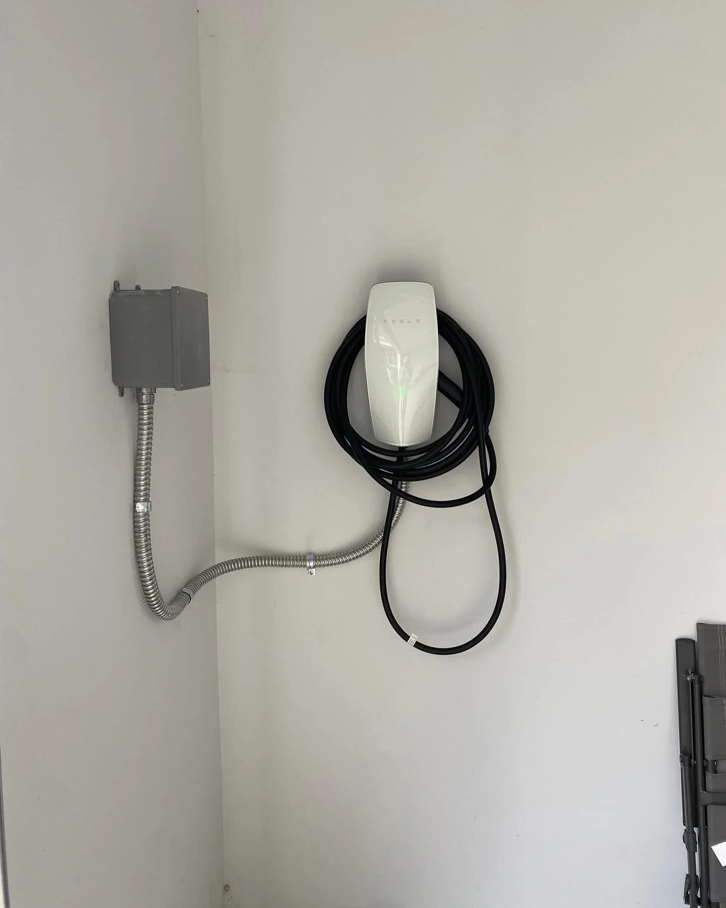 Tesla electric vehicle charging station on a white wall with black cables and grey electrical box.