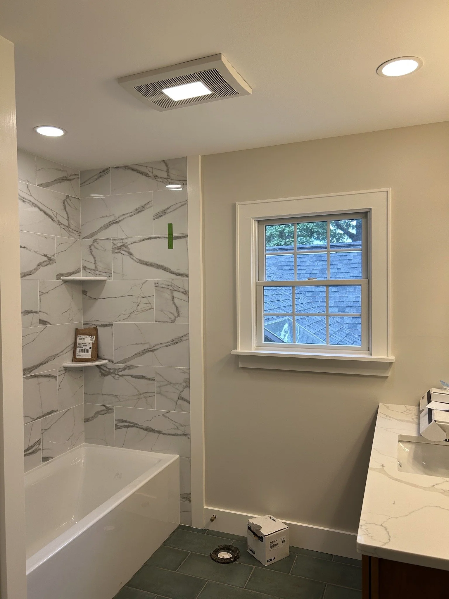 New bathroom with a bathtub, a window, and marble-patterned tiles in the shower area.