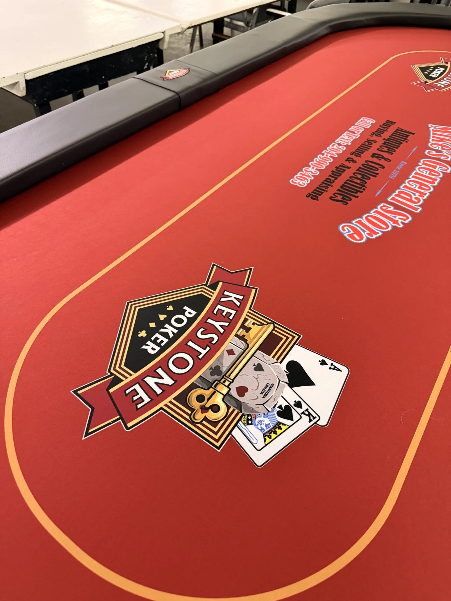 Red poker table with a black padded edge, featuring a colorful poker logo, and a set of playing cards spread out on the surface.