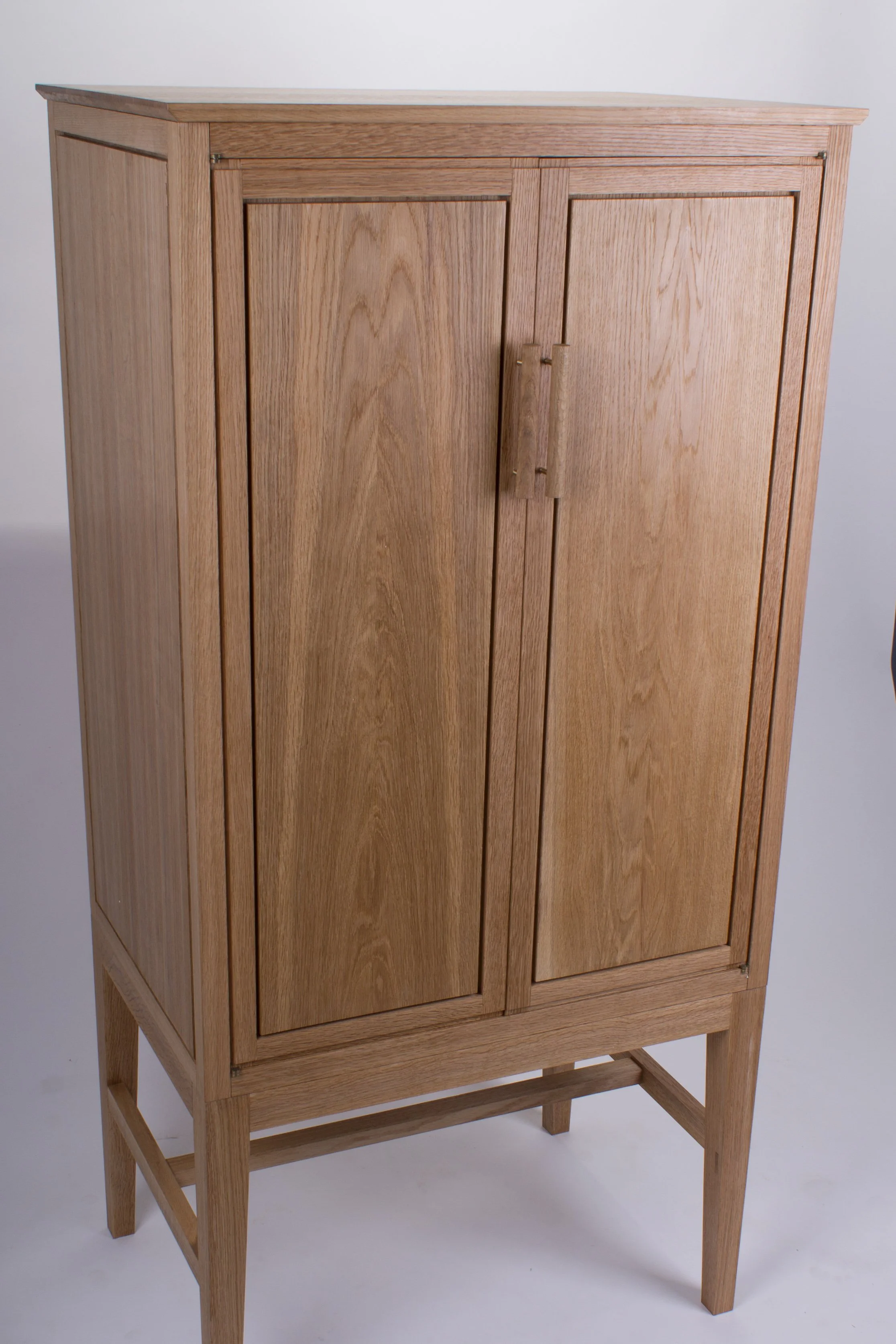 A wooden cabinet with two doors and simple handles, standing on four legs against a plain background.