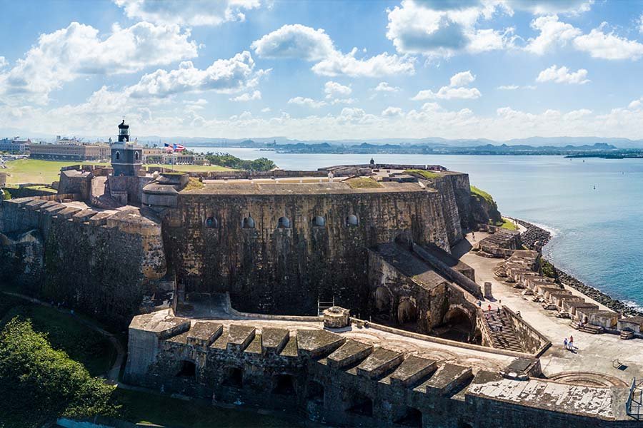 Historic fort on a coastline with water and distant land under a partly cloudy sky.
