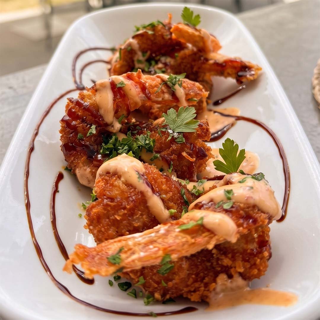 Fried chicken wings topped with creamy sauce and garnished with fresh parsley, served on a white rectangular plate with a drizzle of dark sauce.