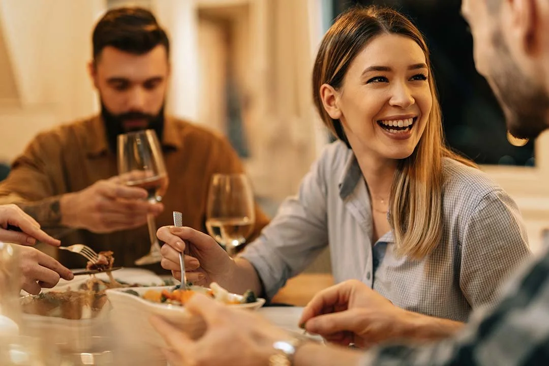 People enjoying a meal together at a restaurant, smiling and engaging in conversation with glasses of wine on the table.