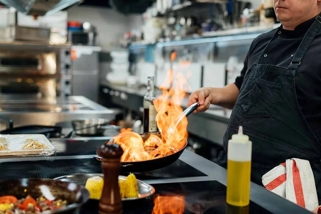 Chef cooking with flames in a professional kitchen.