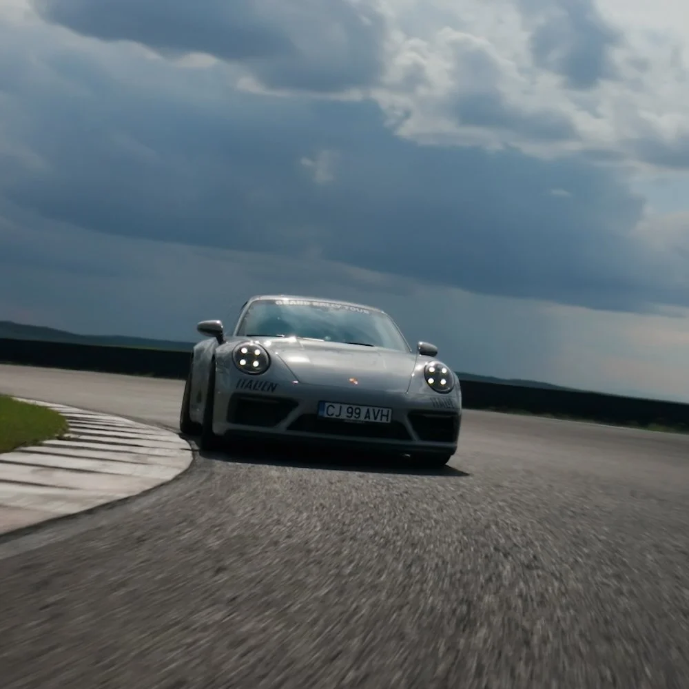 A silver Porsche sports car driving on a race track under dark, cloudy skies.