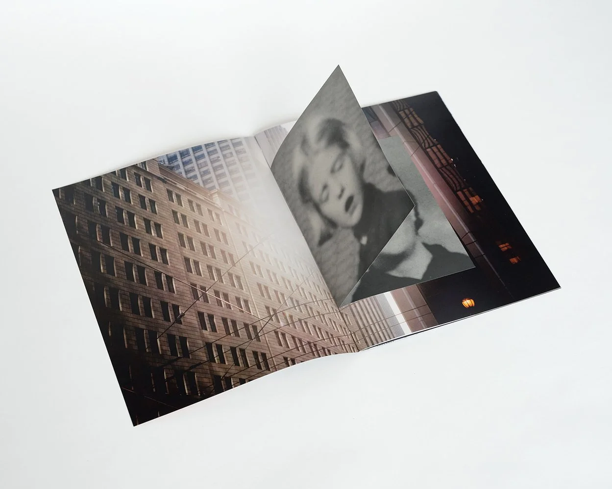 A folded photograph featuring an urban building facade with multiple windows and a blurred black-and-white portrait of a woman.