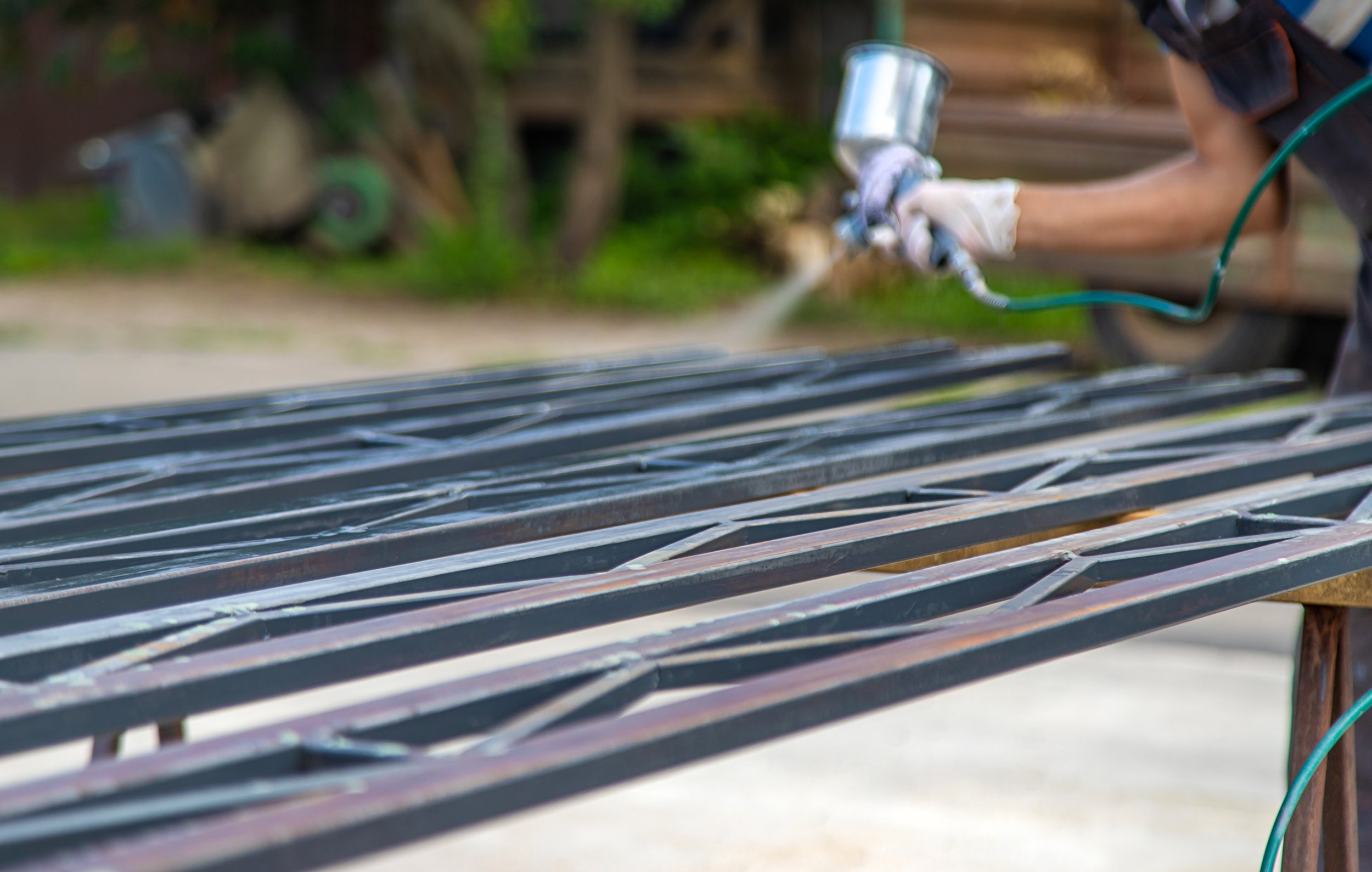 A person spraying a protective coating onto metal bars outdoors, wearing gloves.
