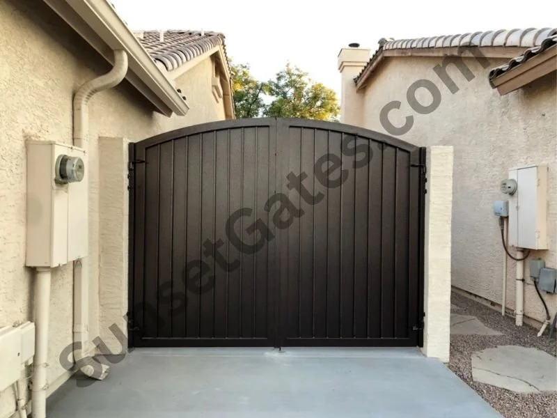 Black arched wooden gate between two beige stucco houses with electrical boxes on the walls