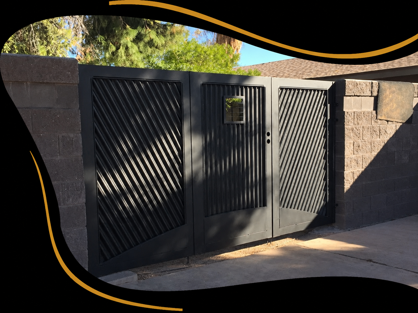 Black metal gate with diagonal slats, a small square window on the right panel, flanked by brick columns, and a beige tackle box on the right side, with trees and a house roof in the background.