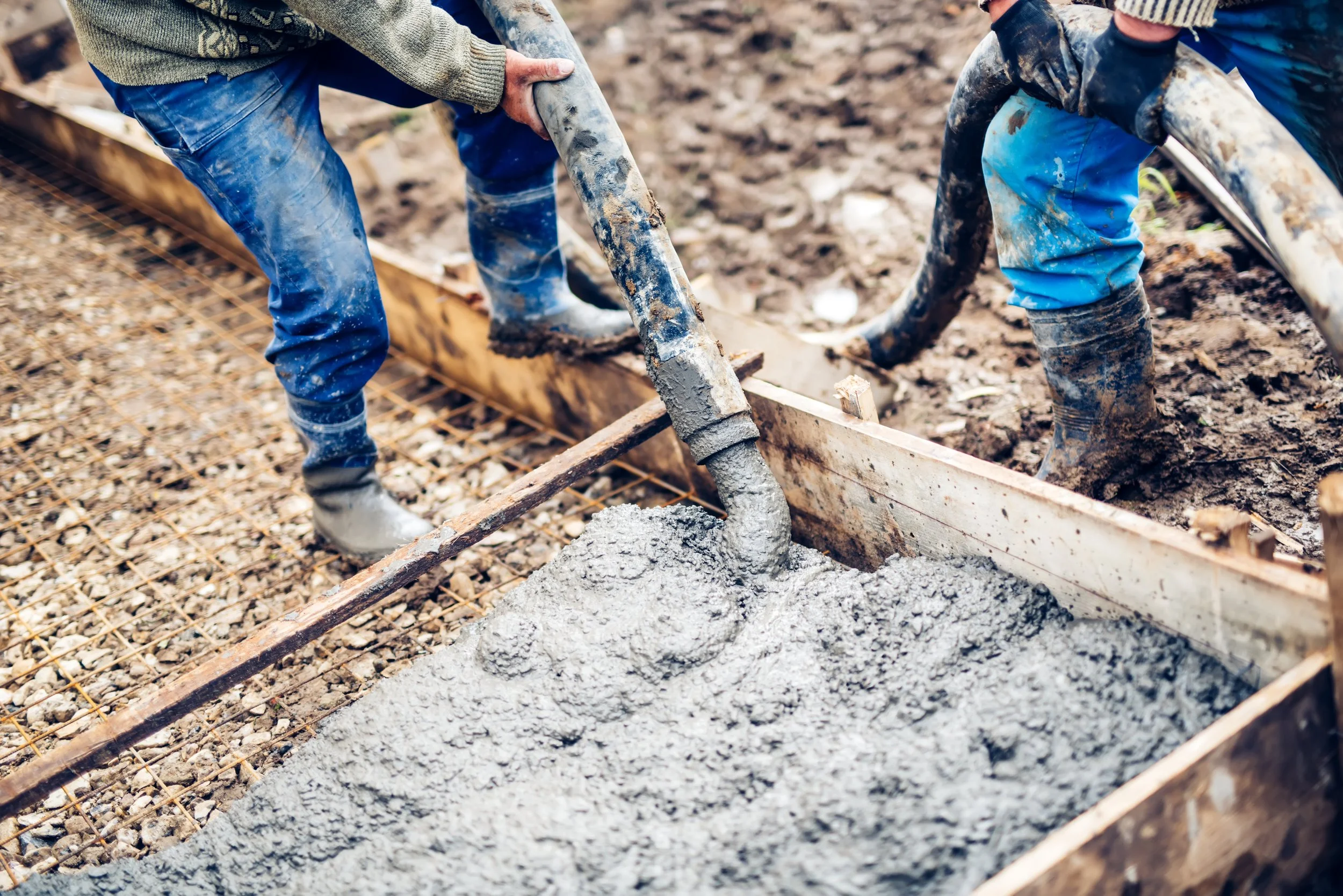Two construction workers kneading wet concrete within a wooden framework on a building site.