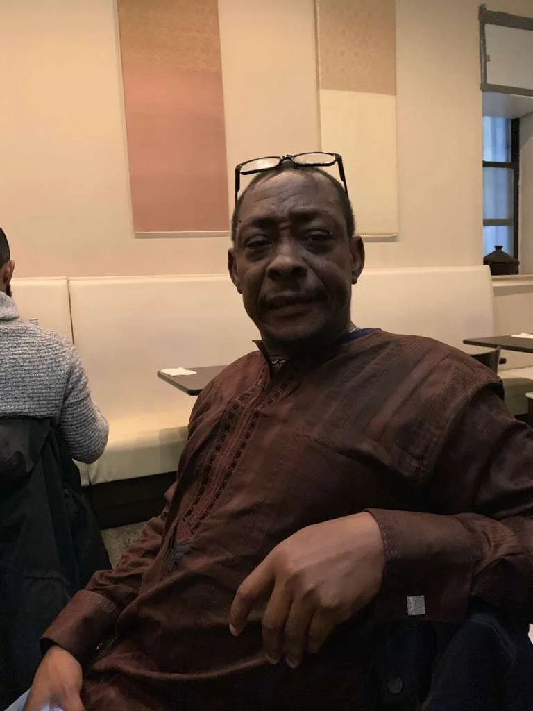 Man sitting in a restaurant with glasses on his head, wearing a brown shirt, and looking at the camera.
