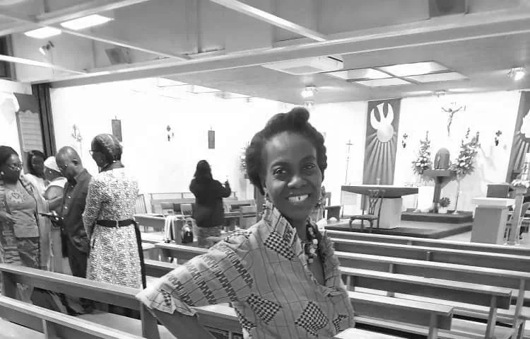 A woman smiling in a church or religious setting with pews, religious symbols, and an altar in the background.