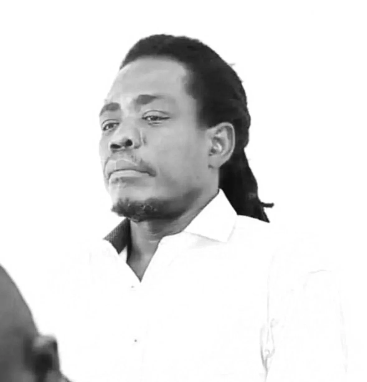 Black and white portrait of a man with long hair tied back, dressed in a white shirt with an open collar, looking to the side with a serious expression.
