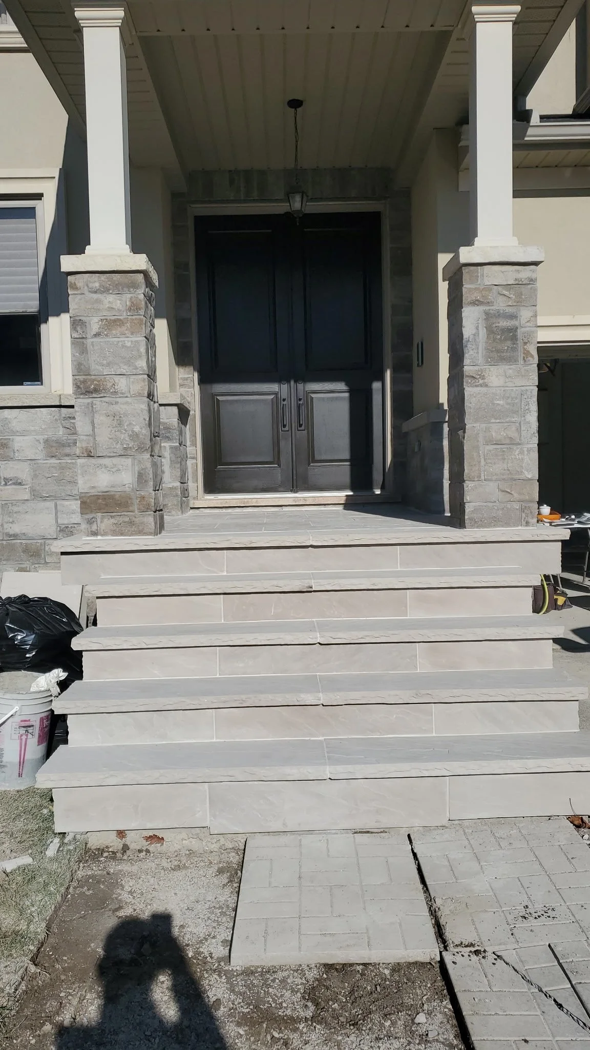 Front porch of a house under construction with steps leading up to a double door, stone columns, and a screened-in porch ceiling.