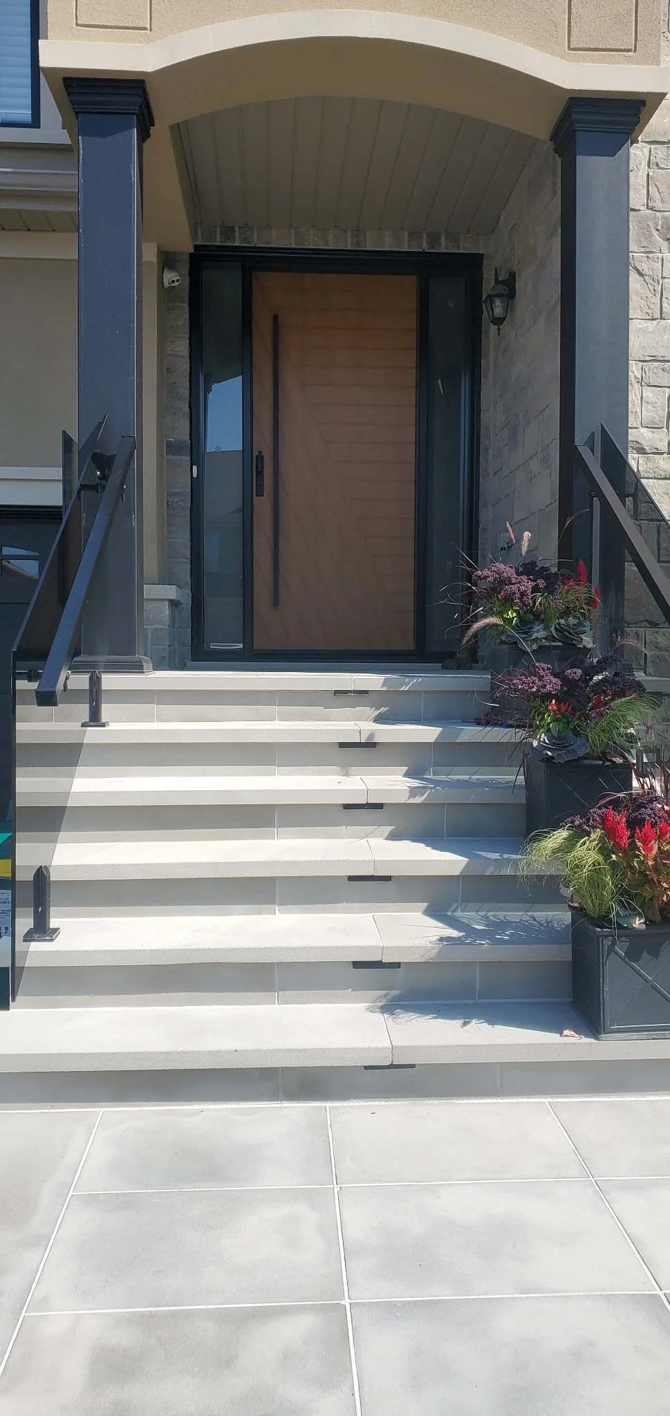 Front entrance with stairs, black railings, a wooden door, and potted plants with flowers.