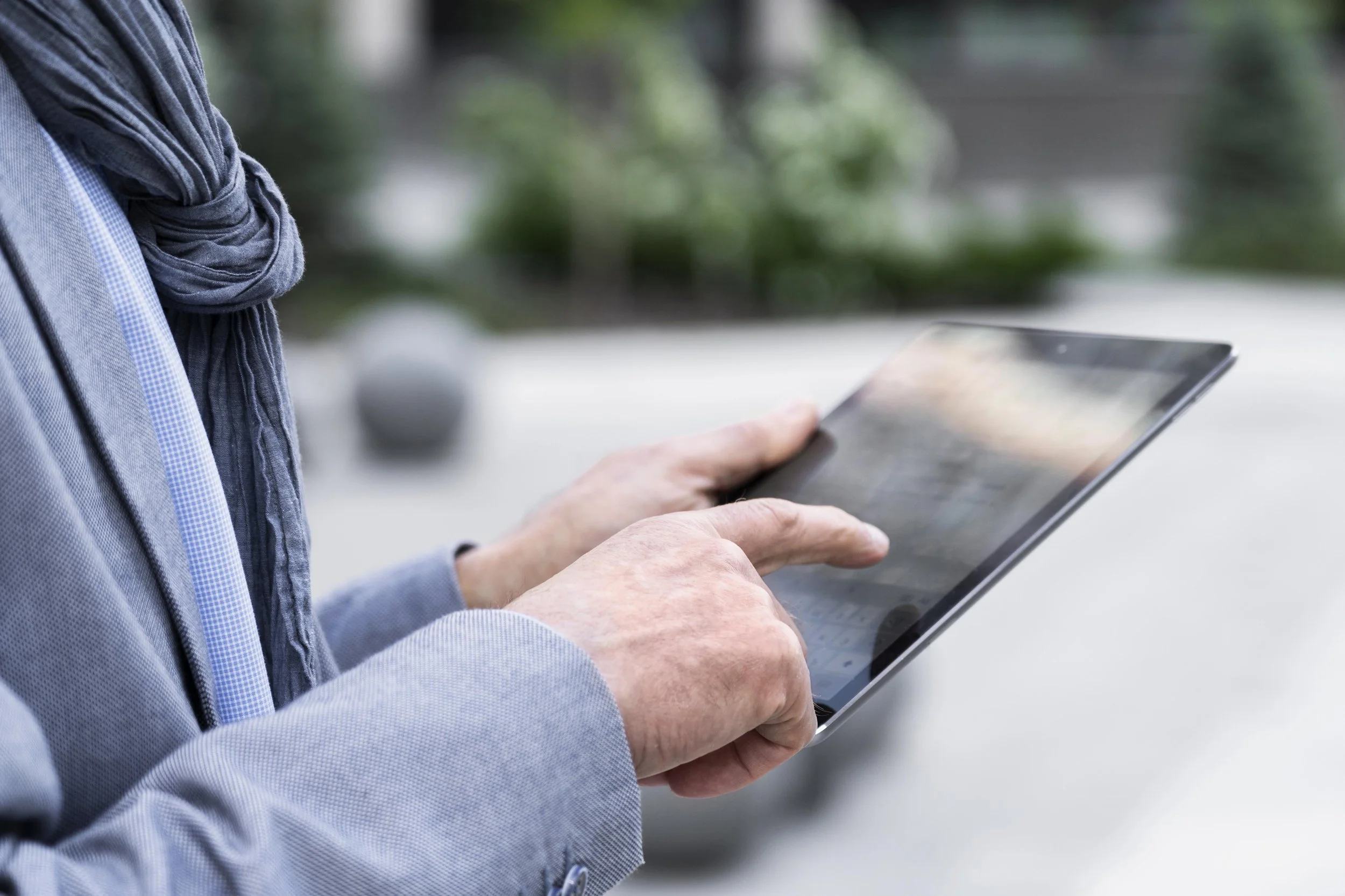 Une personne en blouse bleue utilisant une tablette tactile dans un environnement médical, avec des personnes en blouse blanche en arrière-plan.
