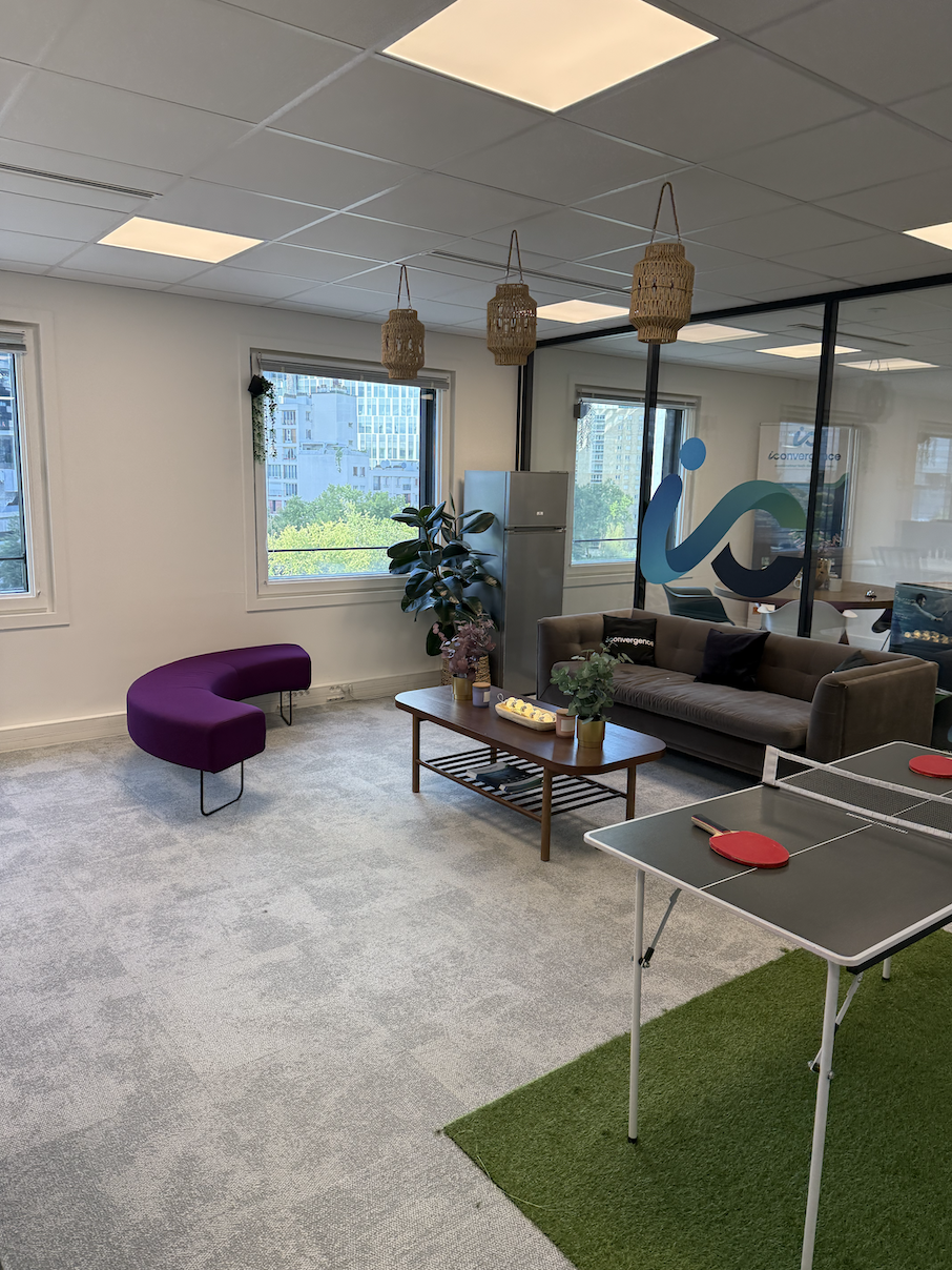 Salon de bureau avec canapé, fauteuil violet, table basse avec plantes, et table de ping-pong.