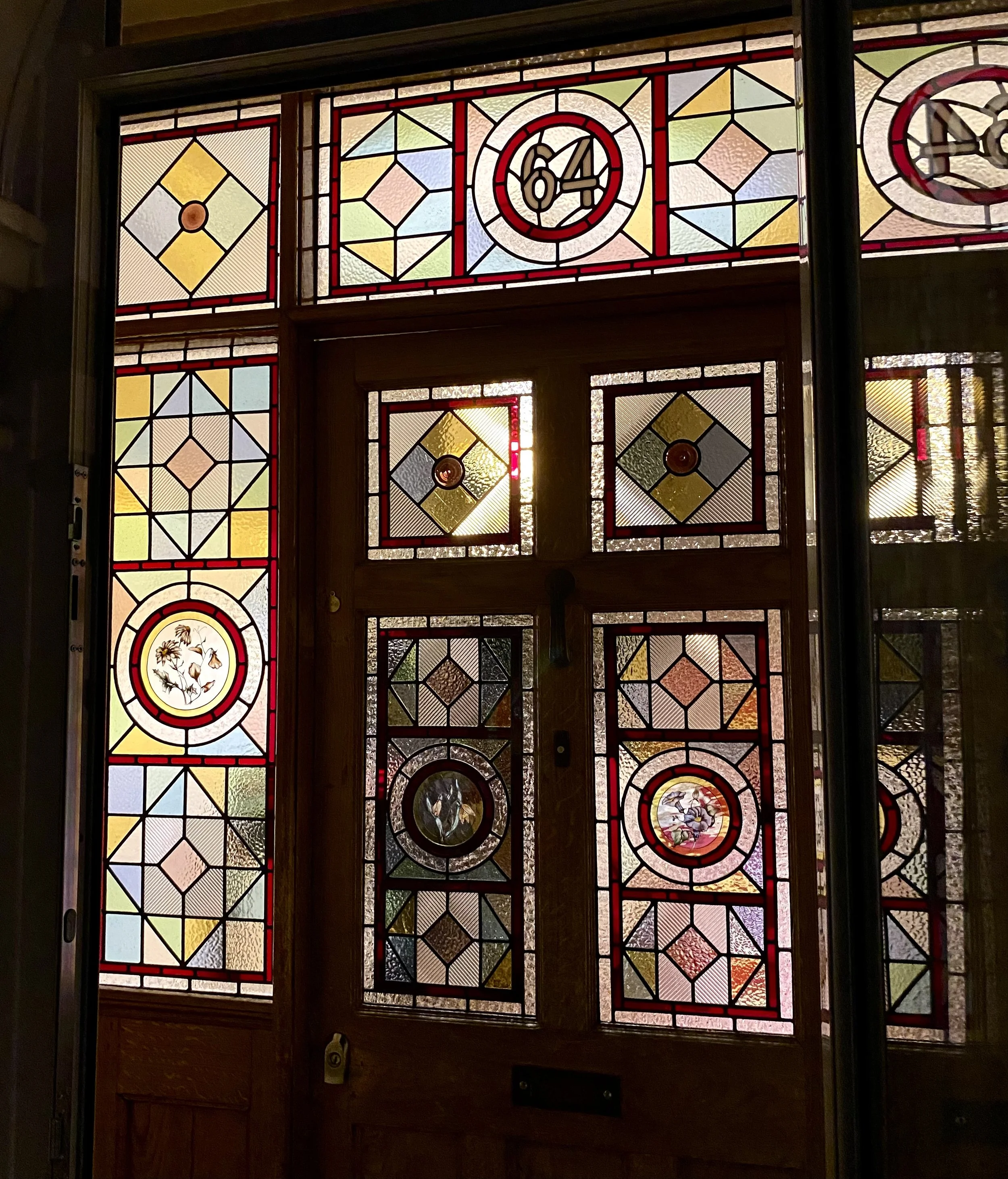 Traditional Colourful stained glass door with various geometric patterns and circular painted roundels, including the number 64 at the top center. Recommended stained glass maker in south east london