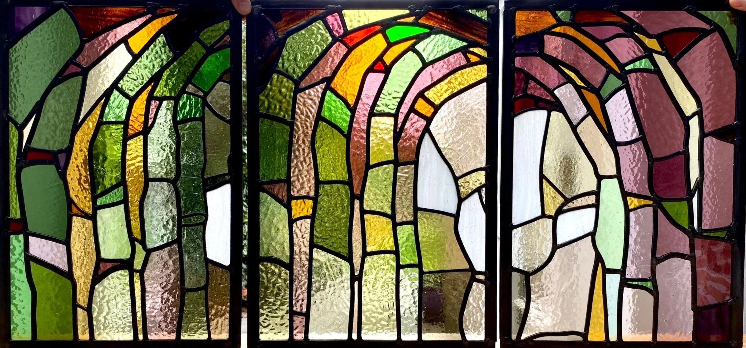 Colorful stained glass window with abstract geometric shapes in green, yellow, pink, orange, and white.  Highly recommended stained glass artist london