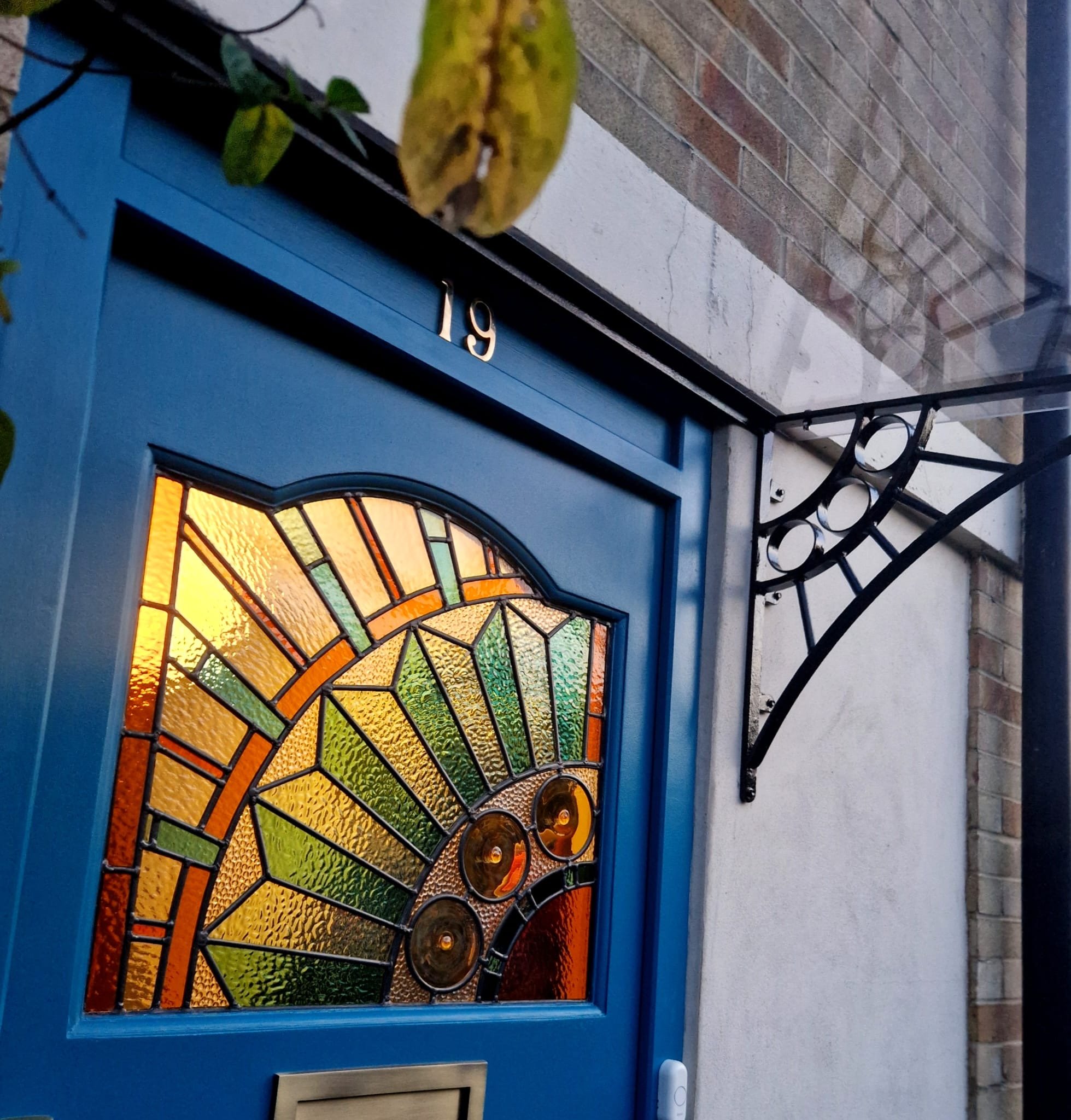 Best stained glass A blue front door with a stained glass window featuring an alternative and fresh interpretation of the classic sunburst design, commissioned for South East London Brockley Lewisham area.  Featuring a decorative black metal awing