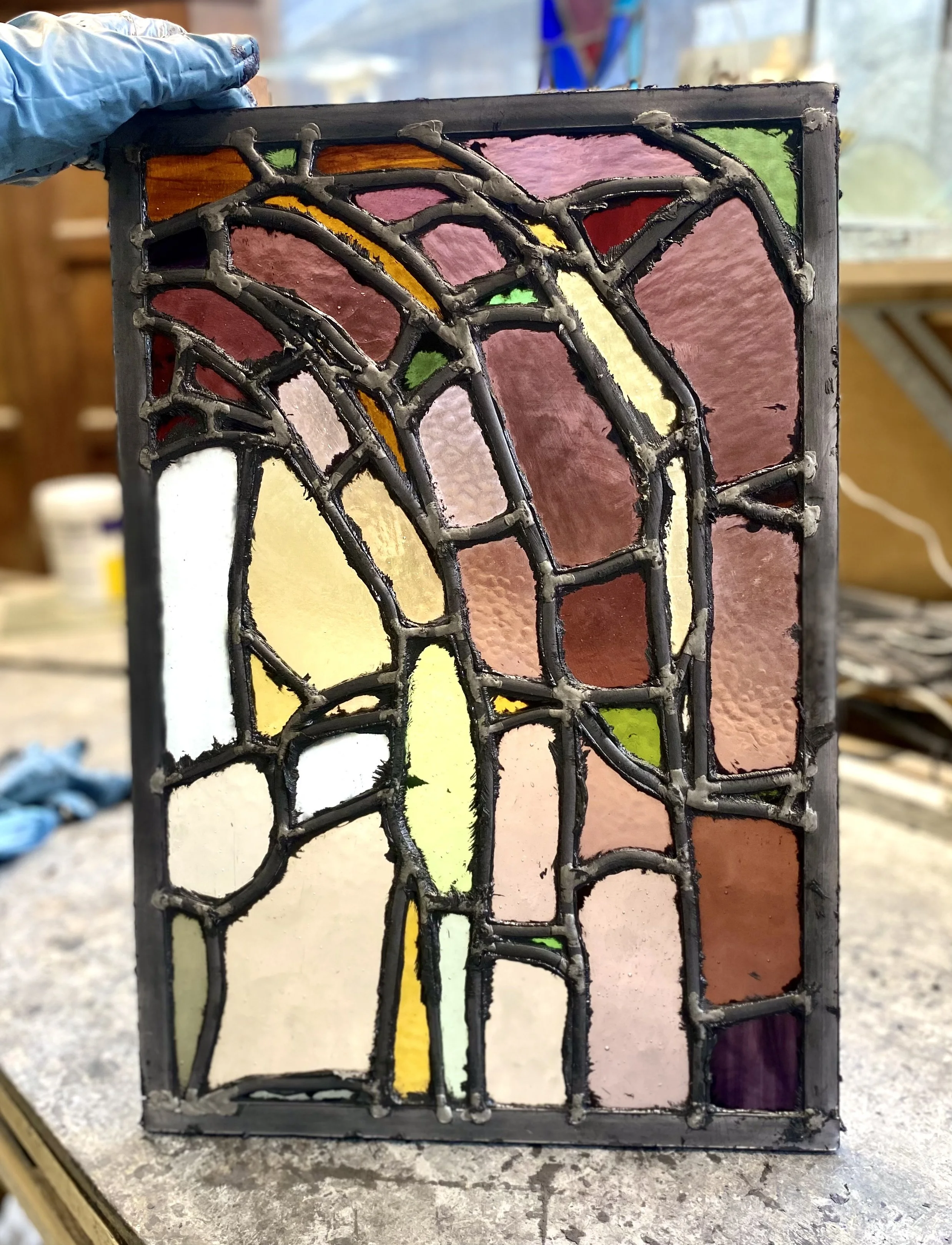 Close-up of a stained glass panel with various irregularly shaped, colorful glass pieces held together by metal cames.