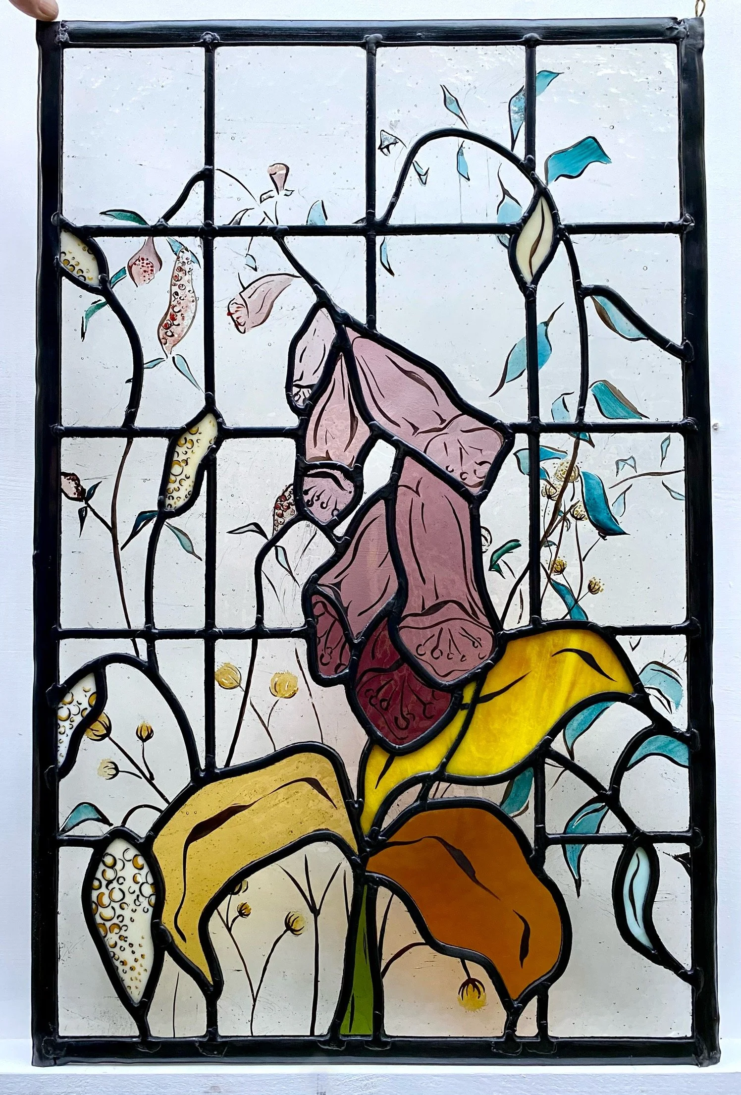 Colorful hand painted stained glass window depicting a pink foxglove flowers with yellow and brown leaves and blue accents built and designed for a bathroom door