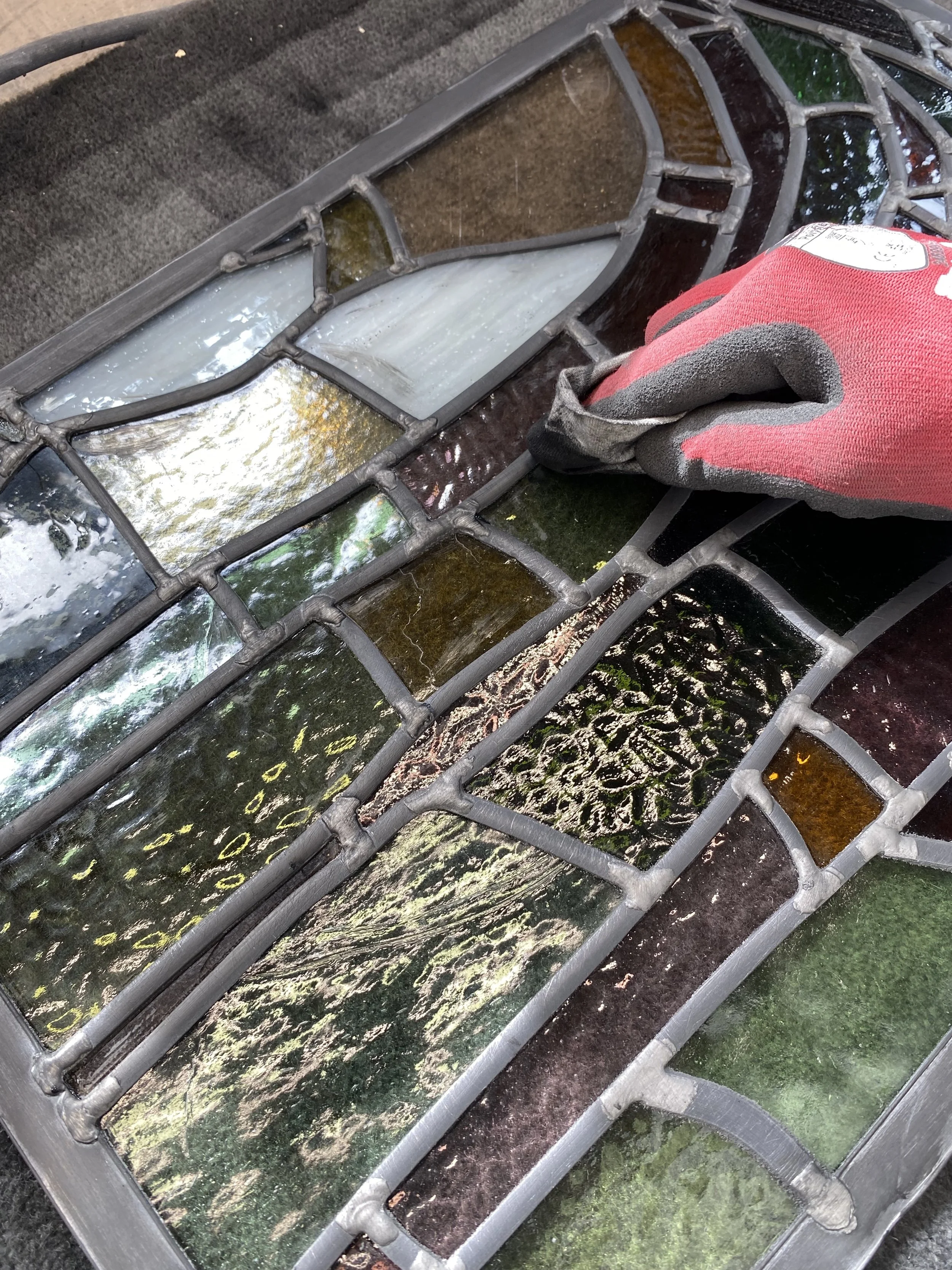 A stained glass window with various colored sections and a person wearing a red glove working on it.