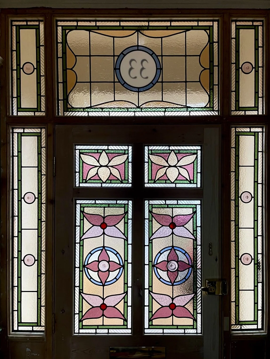 Decorative stained glass window with floral and geometric patterns, featuring pink, green, yellow, white, purple, and blue glass pieces in intricate designs.  Designed and built by Zoe Henderson for the Corbett Estate, Forster Estate in Catford