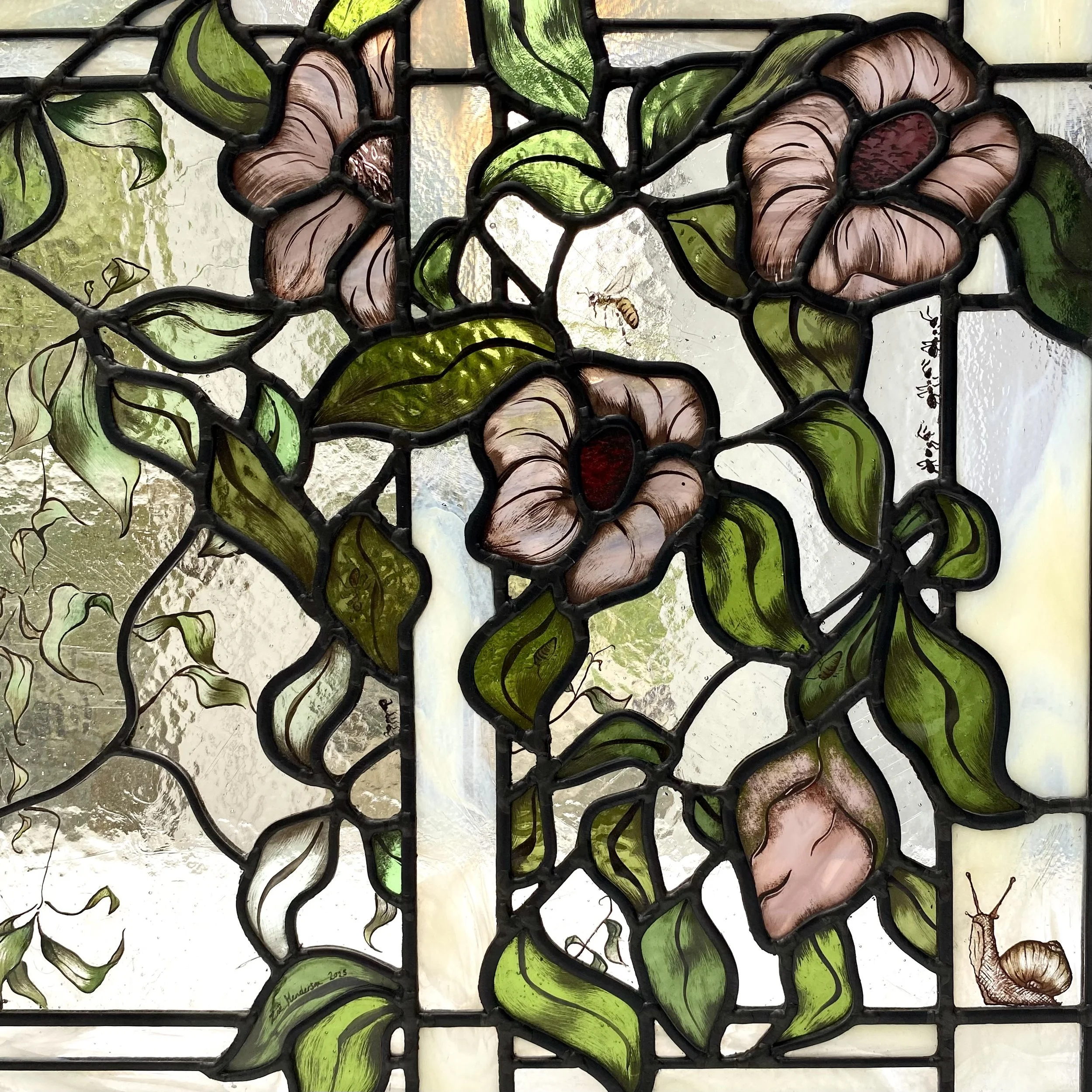 A stained glass window featuring pink roses, green leaves, a snail at the bottom right, and a small bee near the top center, with textured glass and black leading.
