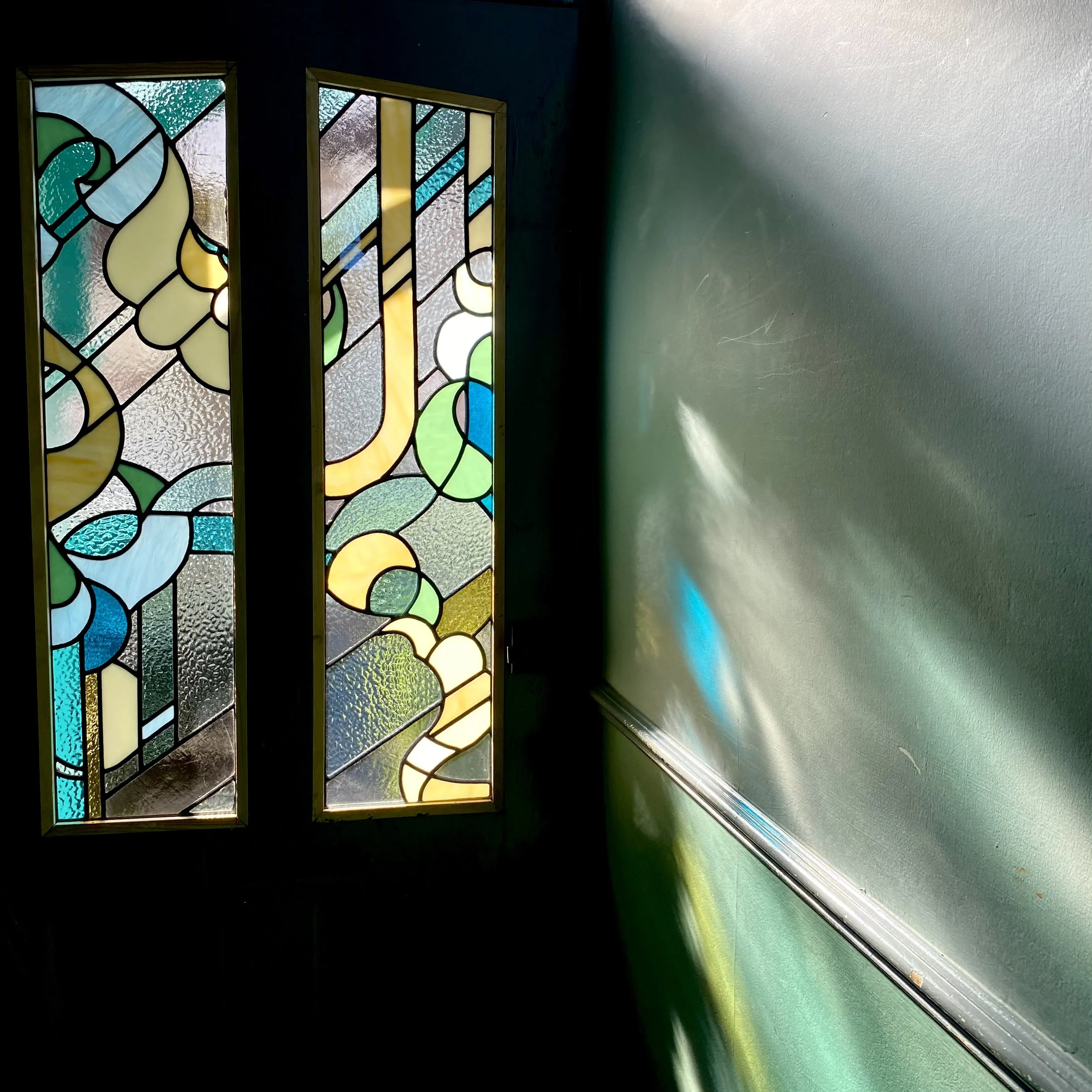 Colorful stained glass window casting different colors of light onto a green wall.