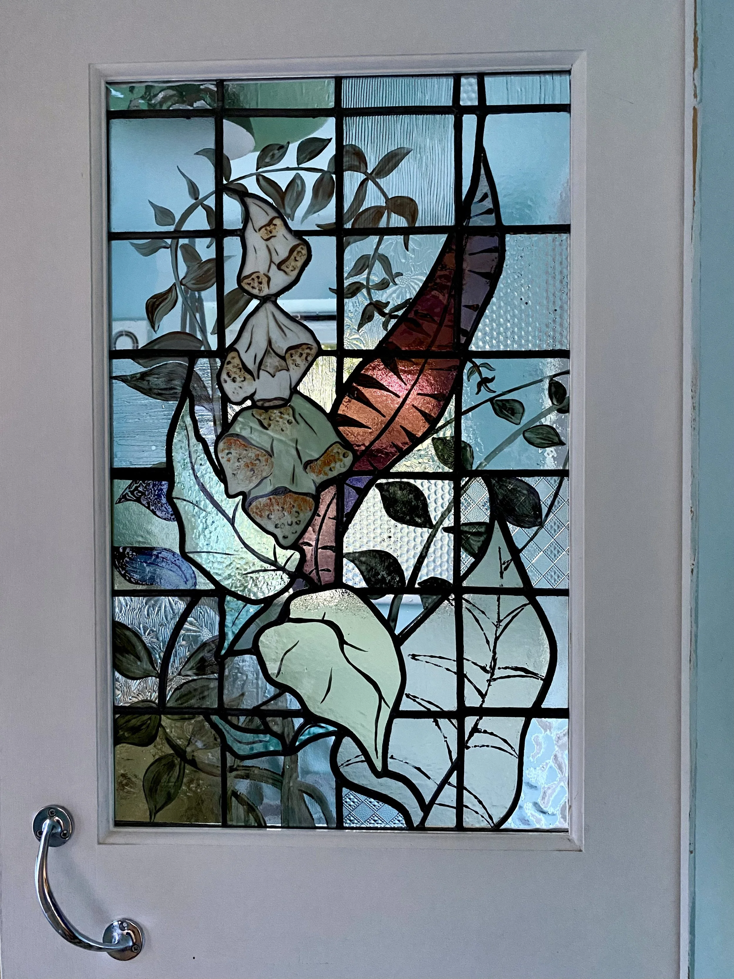 Decorative stained glass window featuring a large flower with pink and purple fox glove flowers, surrounded by various green leaves and branches. Bathroom window