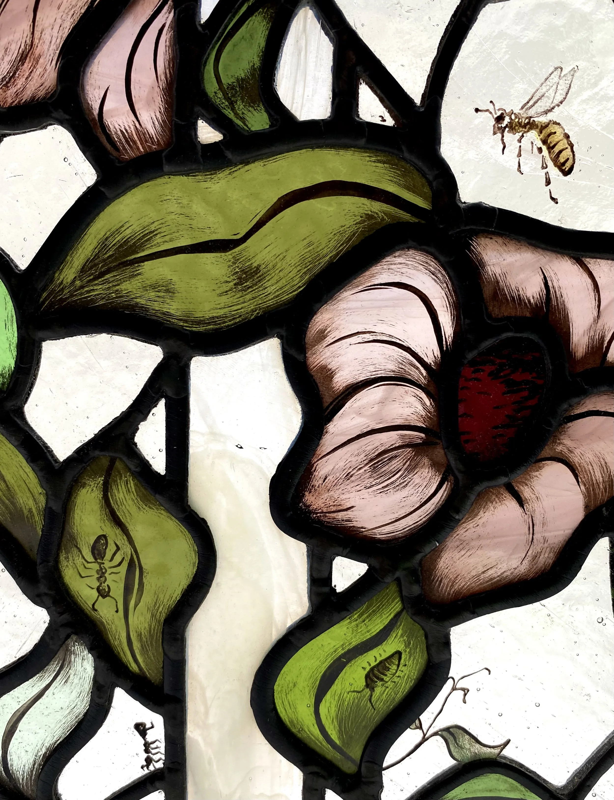 Close-up view of a stained glass art piece featuring vibrant green and pink sections with black outlines, depicting a bee near a yellow flower.