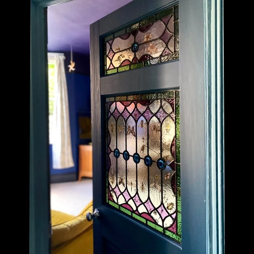 A blue door with internal stained glass window panels featuring coulorful geometric patterns.  Featuring floral and insect designs.
