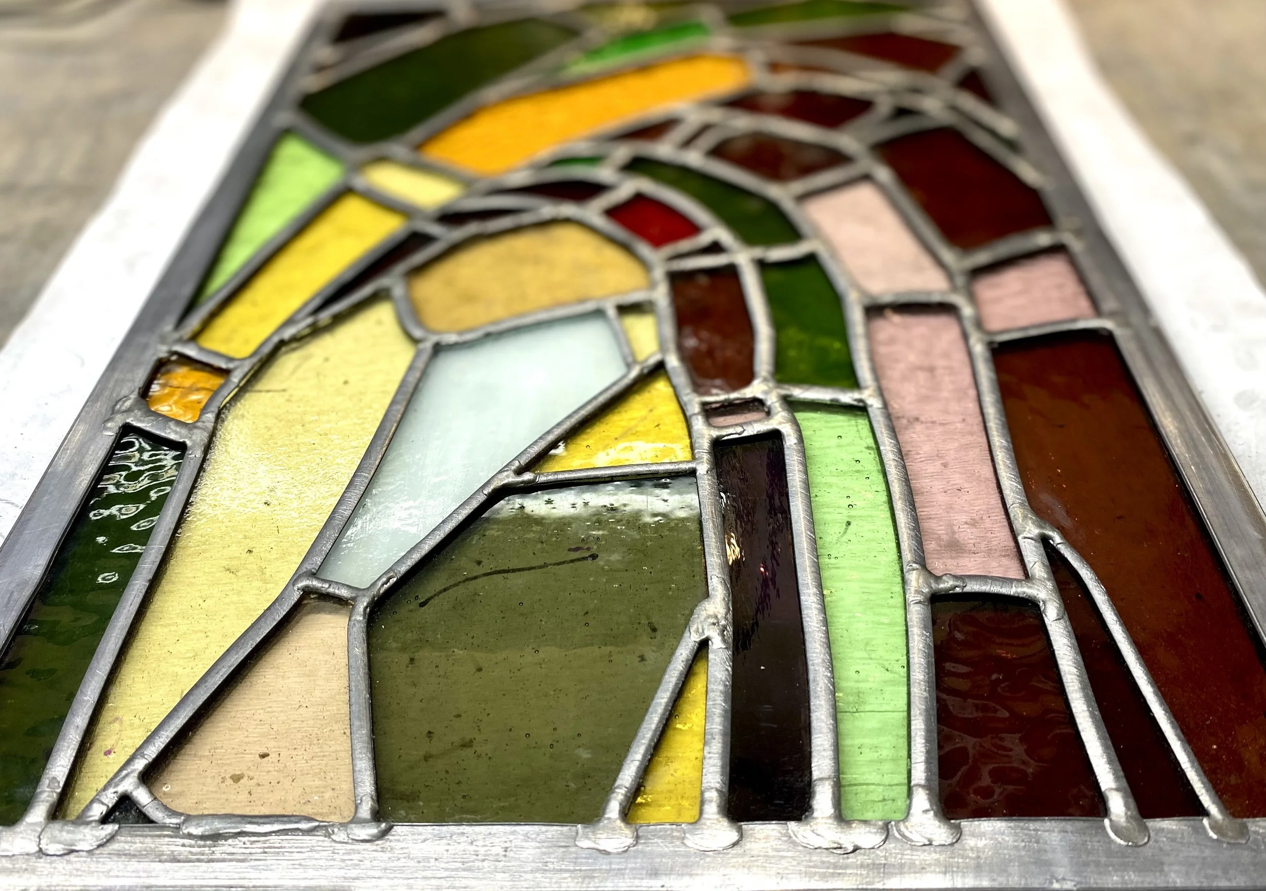 Close-up of a stained glass window with various colored glass pieces in green, yellow, brown, and pink,