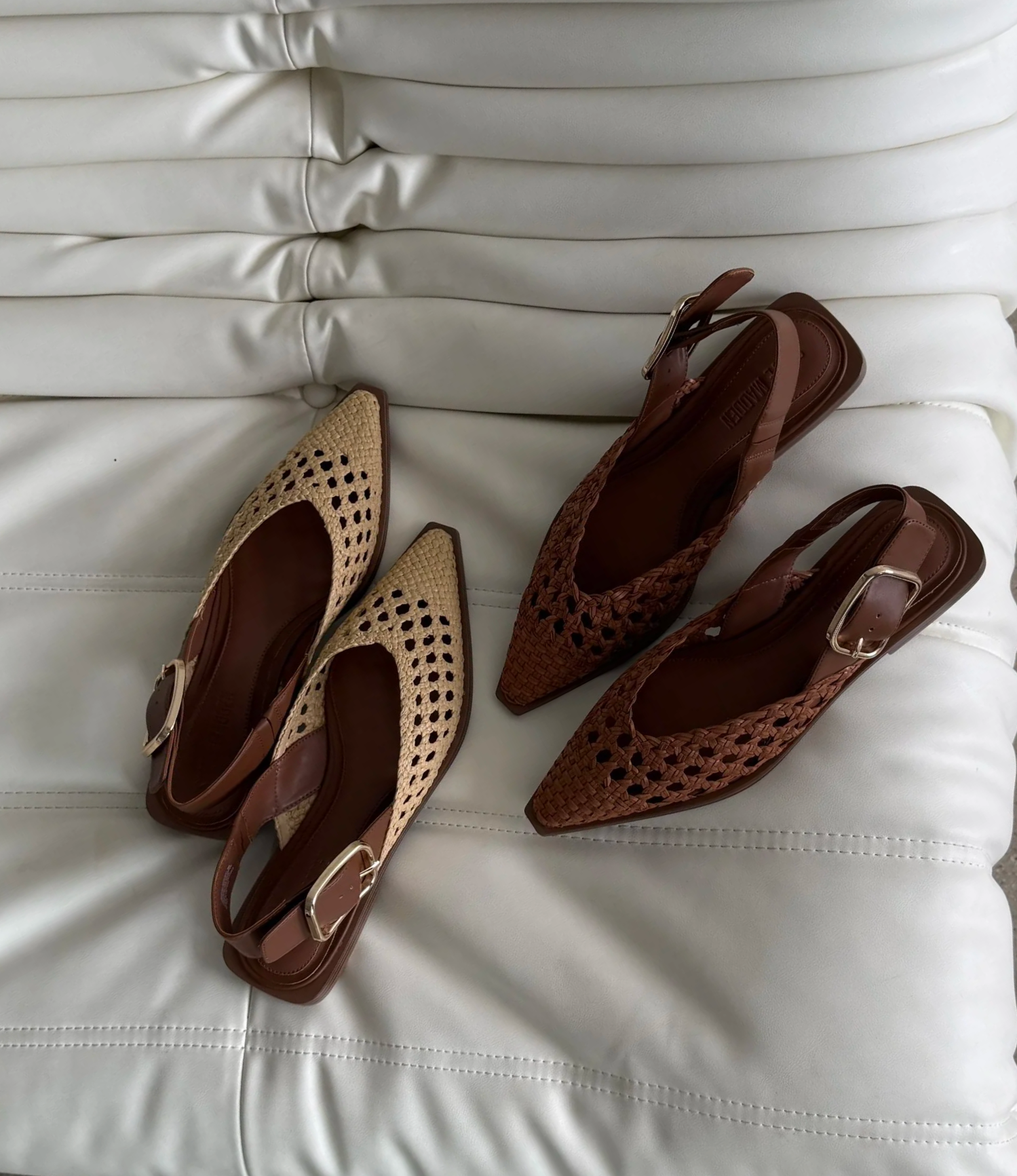 Two pairs of women's heeled shoes with woven and perforated designs, placed on a white leather tufted couch.