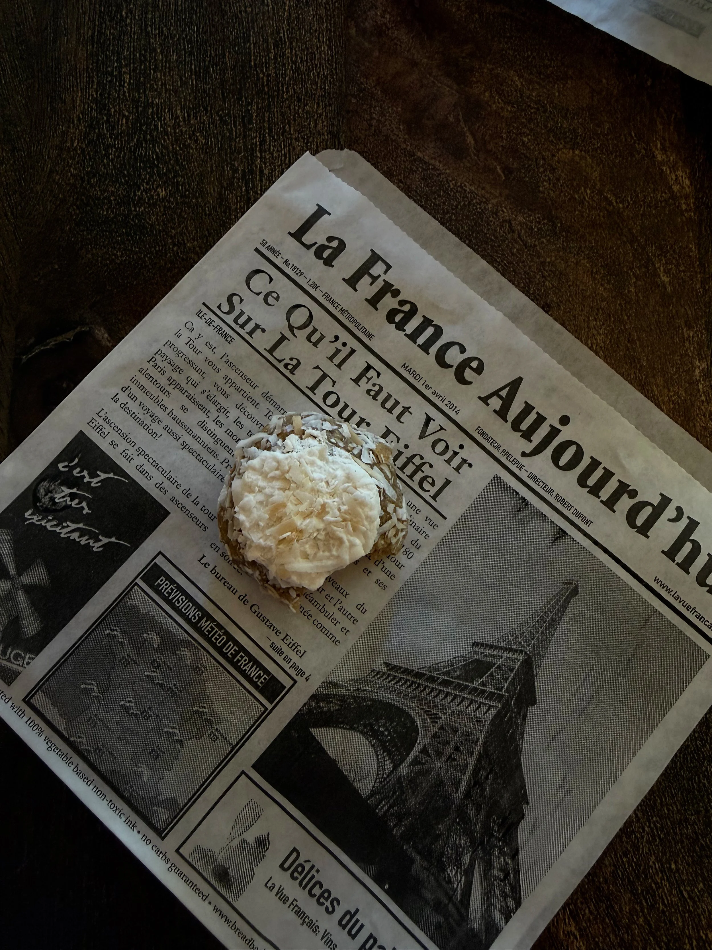 A baking pastry topped with shredded coconut on a French newspaper with an image of the Eiffel Tower.