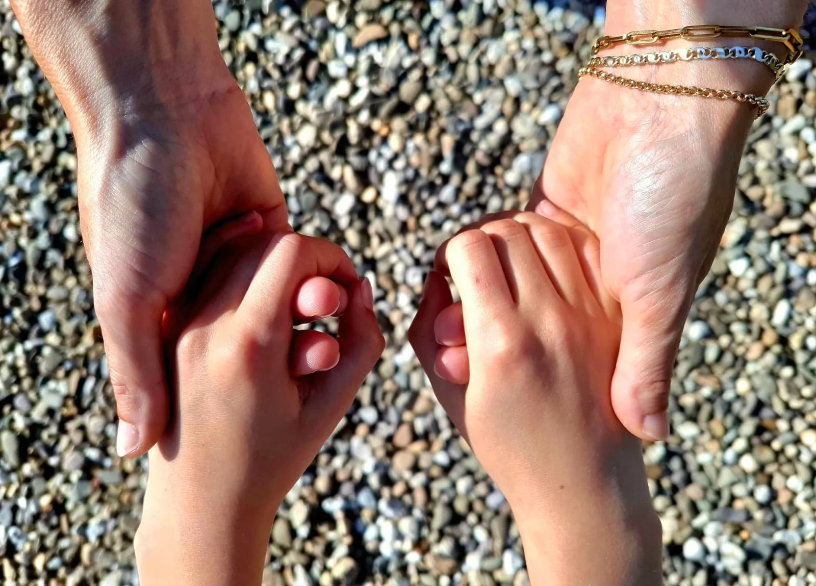 Twee handen, een volwassen hand en een kinderhand, die elkaar vasthouden, met een achtergrond van kiezels.
