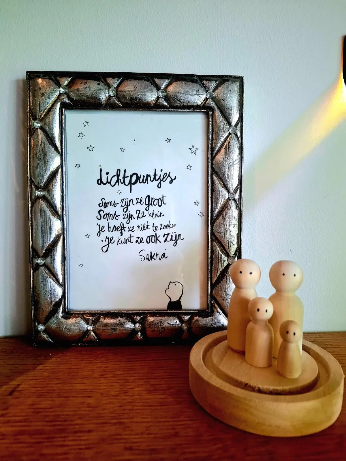 Fotolijst met gedicht en kleine tekening van een hond, naast vier houten poppetjes op een ronde houten schaal.
