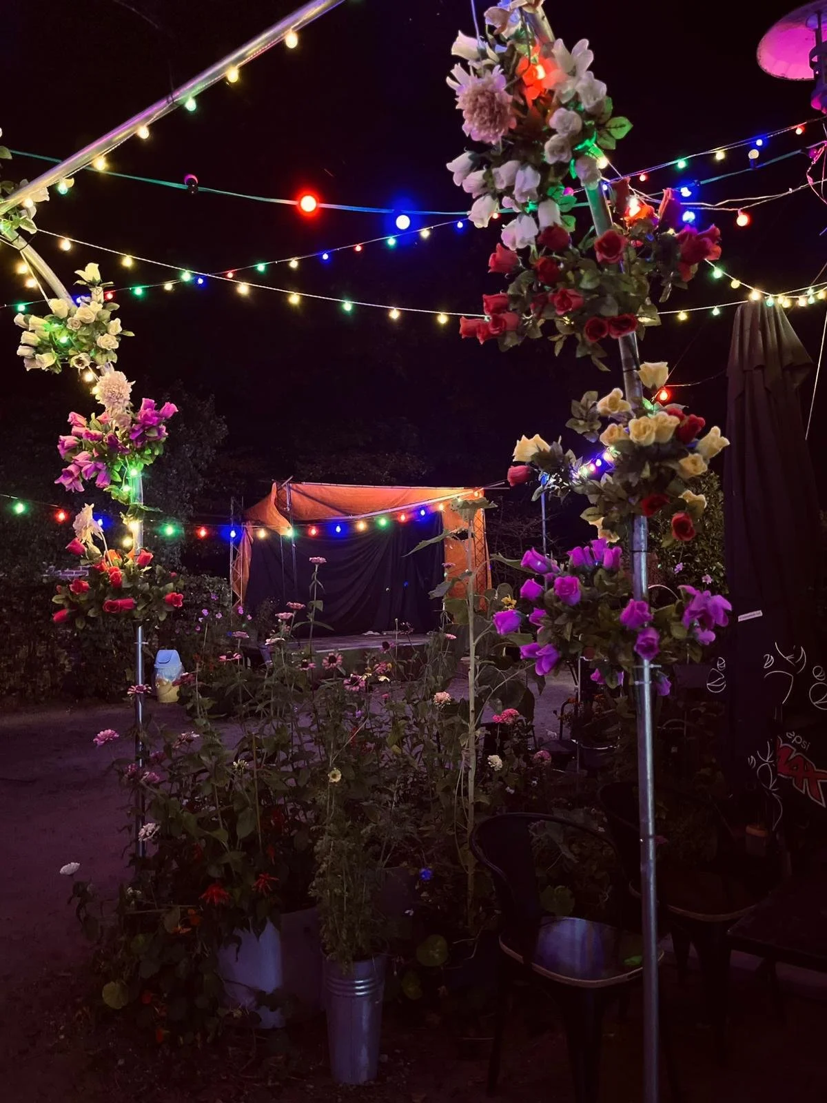 Nighttime outdoor stage decorated with colorful string lights and flower arrangements.