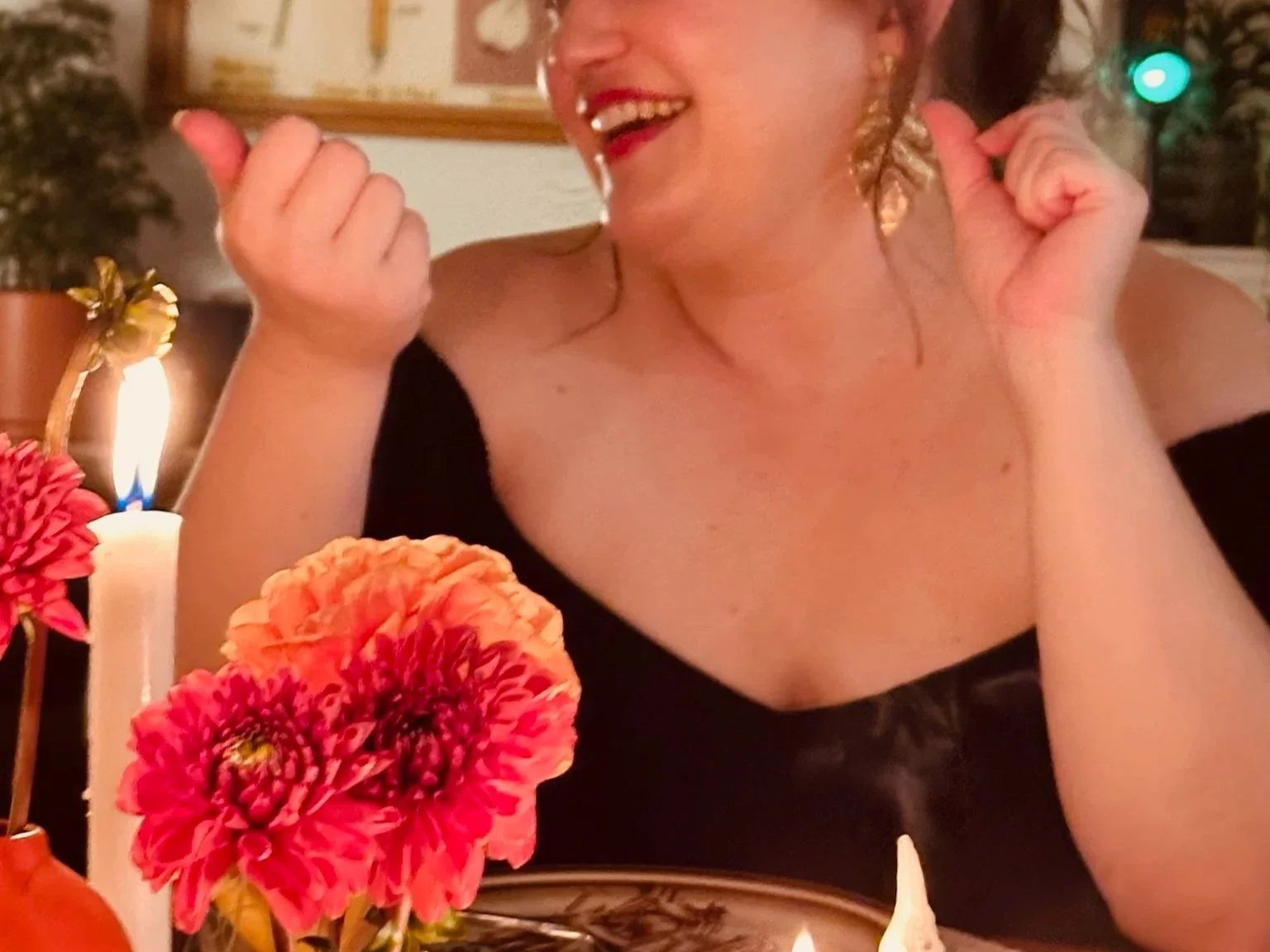 A woman smiling at a birthday celebration with flowers, candles, and a lit birthday cake in front of her.