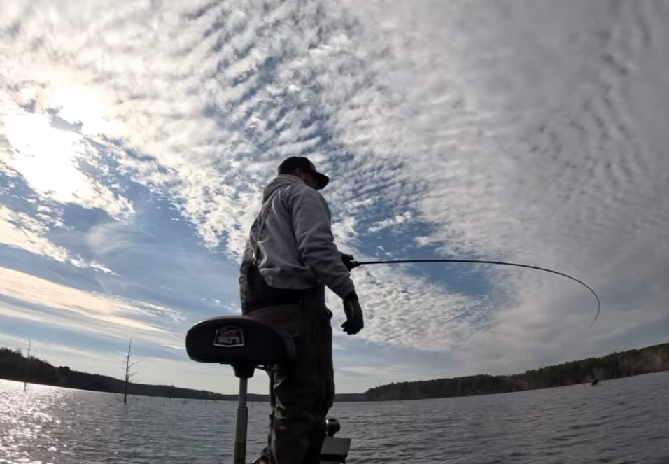 Person fishing from a boat on a lake under a partly cloudy sky