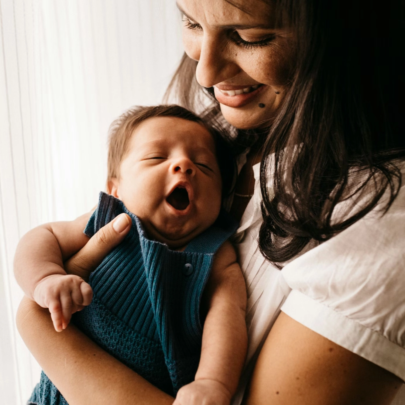 Une femme tient un bébé qui bâille.