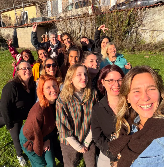 Groupe de personnes souriantes posant à l'extérieur ensoleillé, avec des bâtiments en arrière-plan.