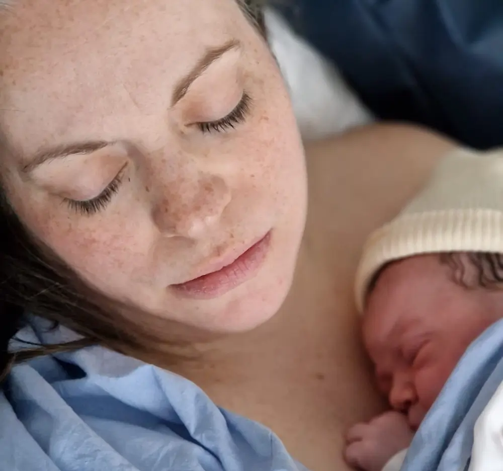 Une mère a les yeux fermés, tenant un nouveau-né contre sa poitrine, tous deux endormis, dans un lit d'hôpital.