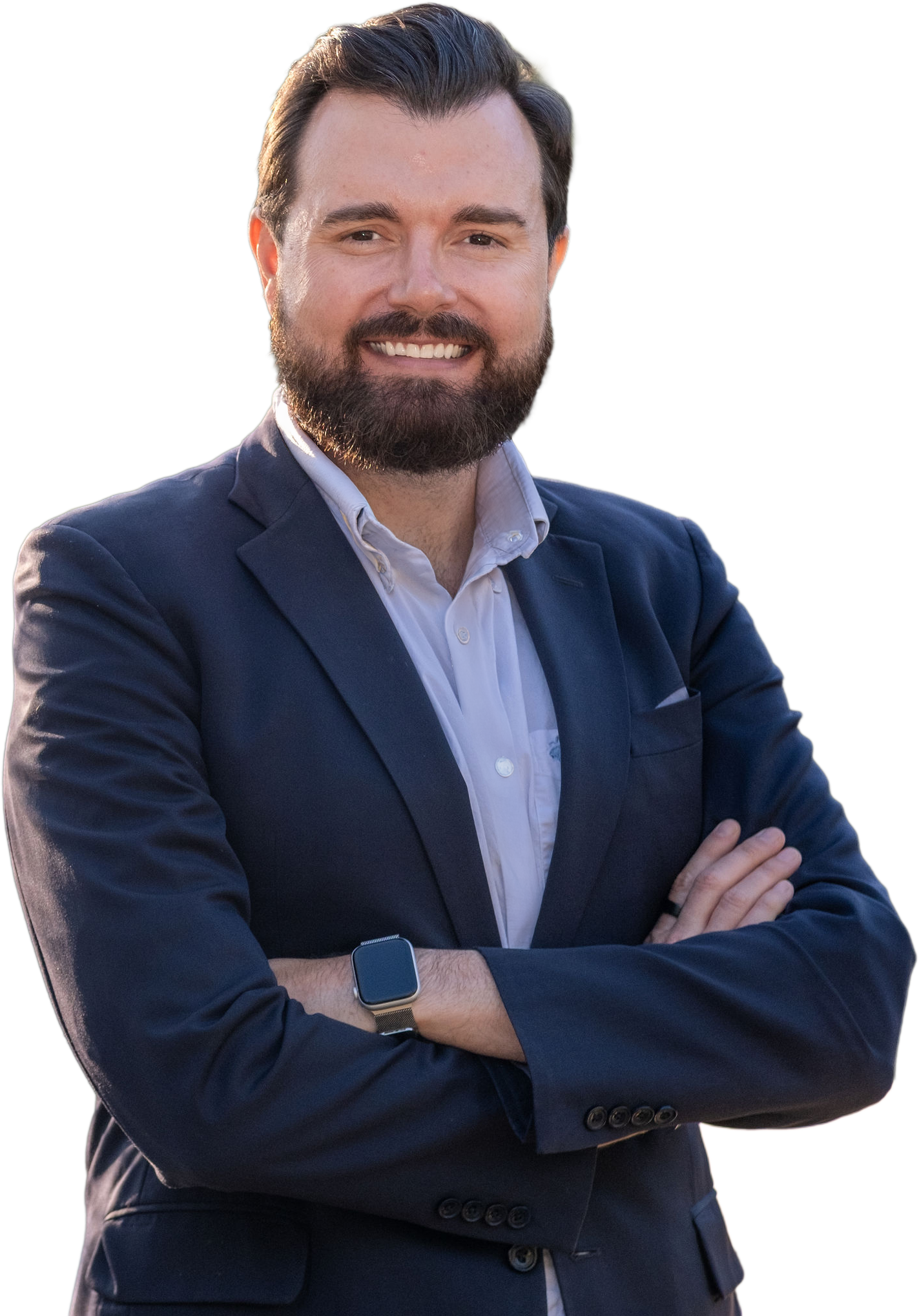 A smiling man with brown hair, a beard, and a mustache, wearing a dark blue blazer, white dress shirt, and a smartwatch, crossing his arms.