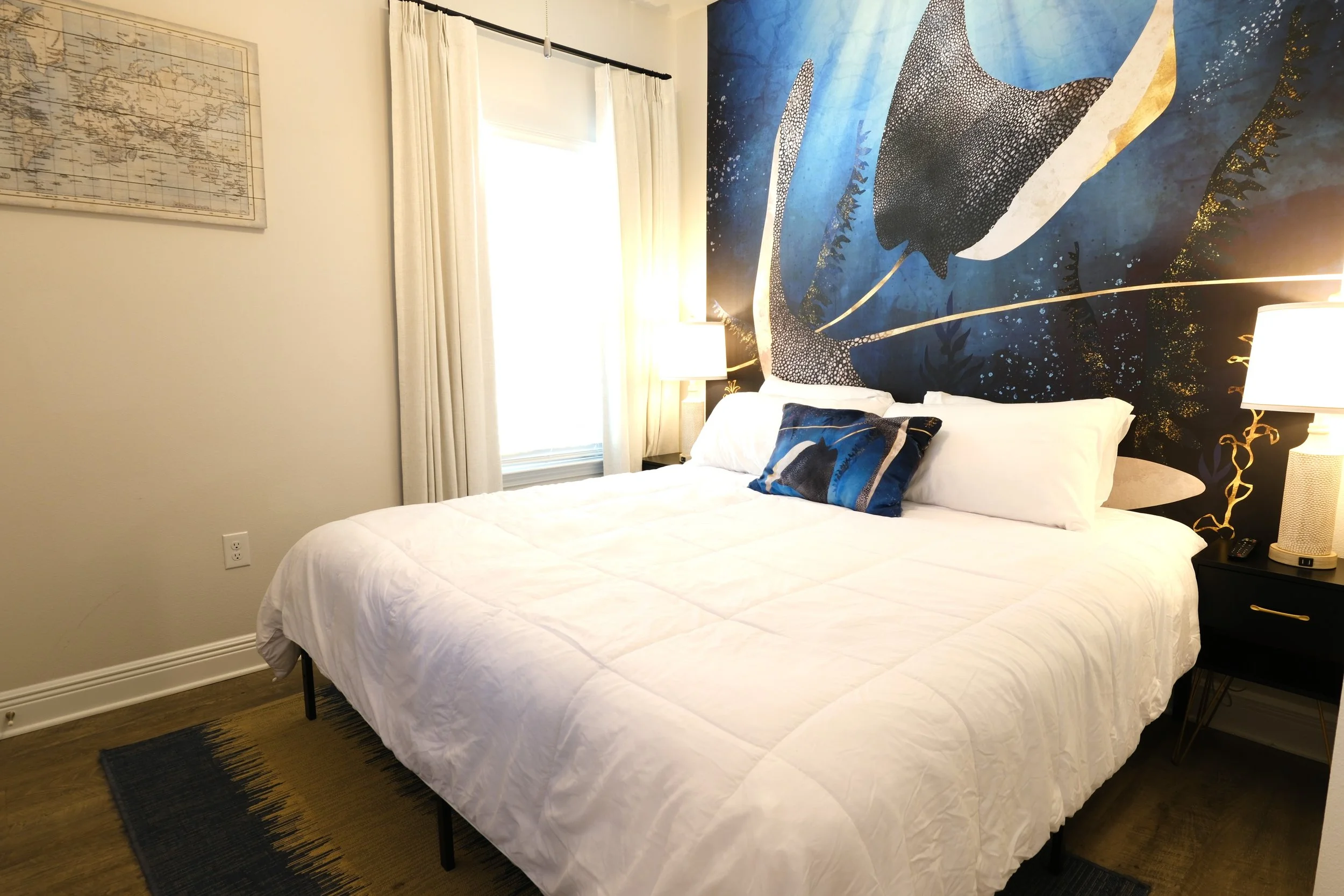 A bedroom with a white bed, ocean-themed mural, and ceiling fan with lights.