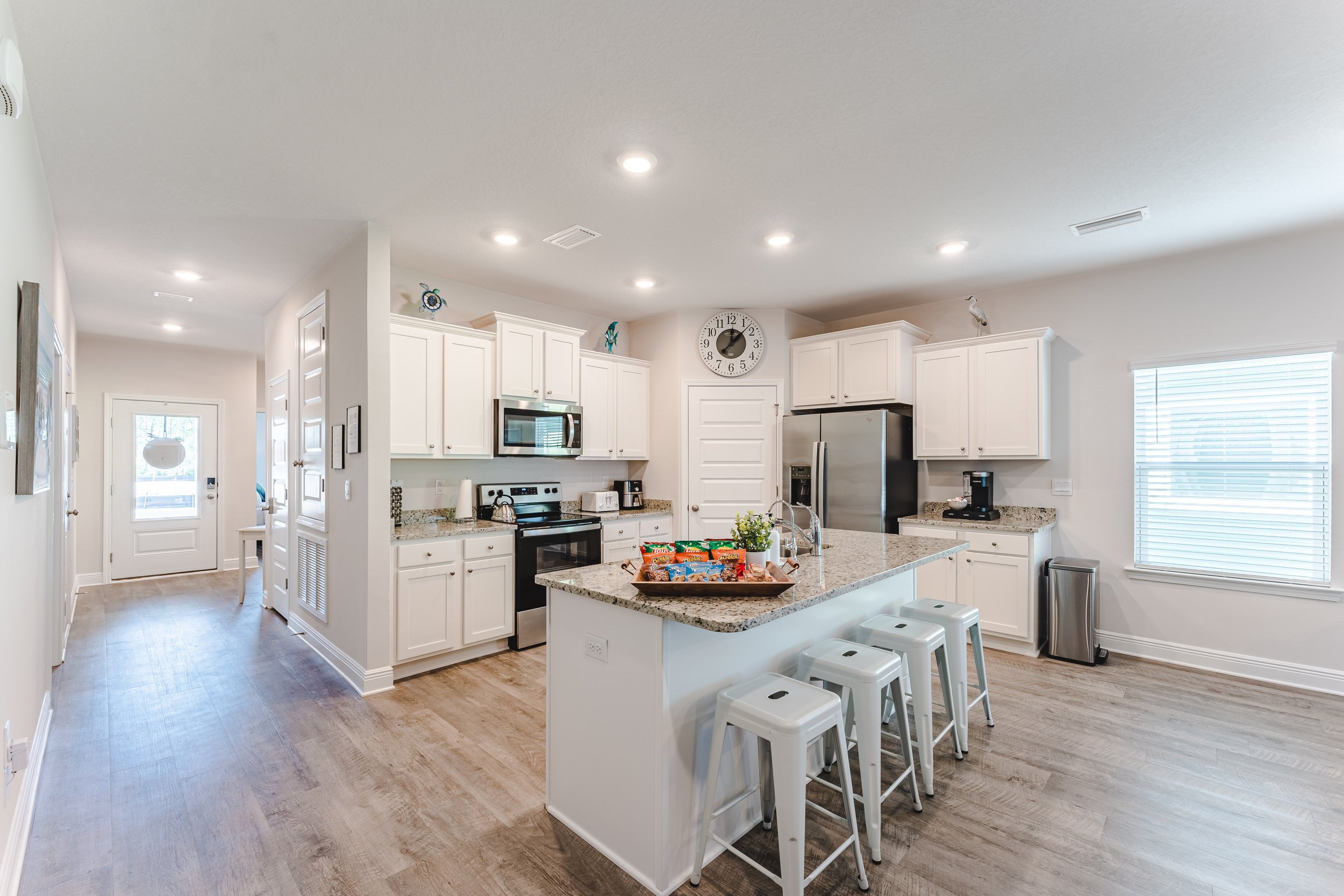 Modern kitchen with white cabinets, stainless steel appliances, granite countertops, island with bar stools, and a clock on the wall.