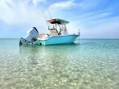 A white motorboat anchored in shallow clear turquoise water near a sandy beach.