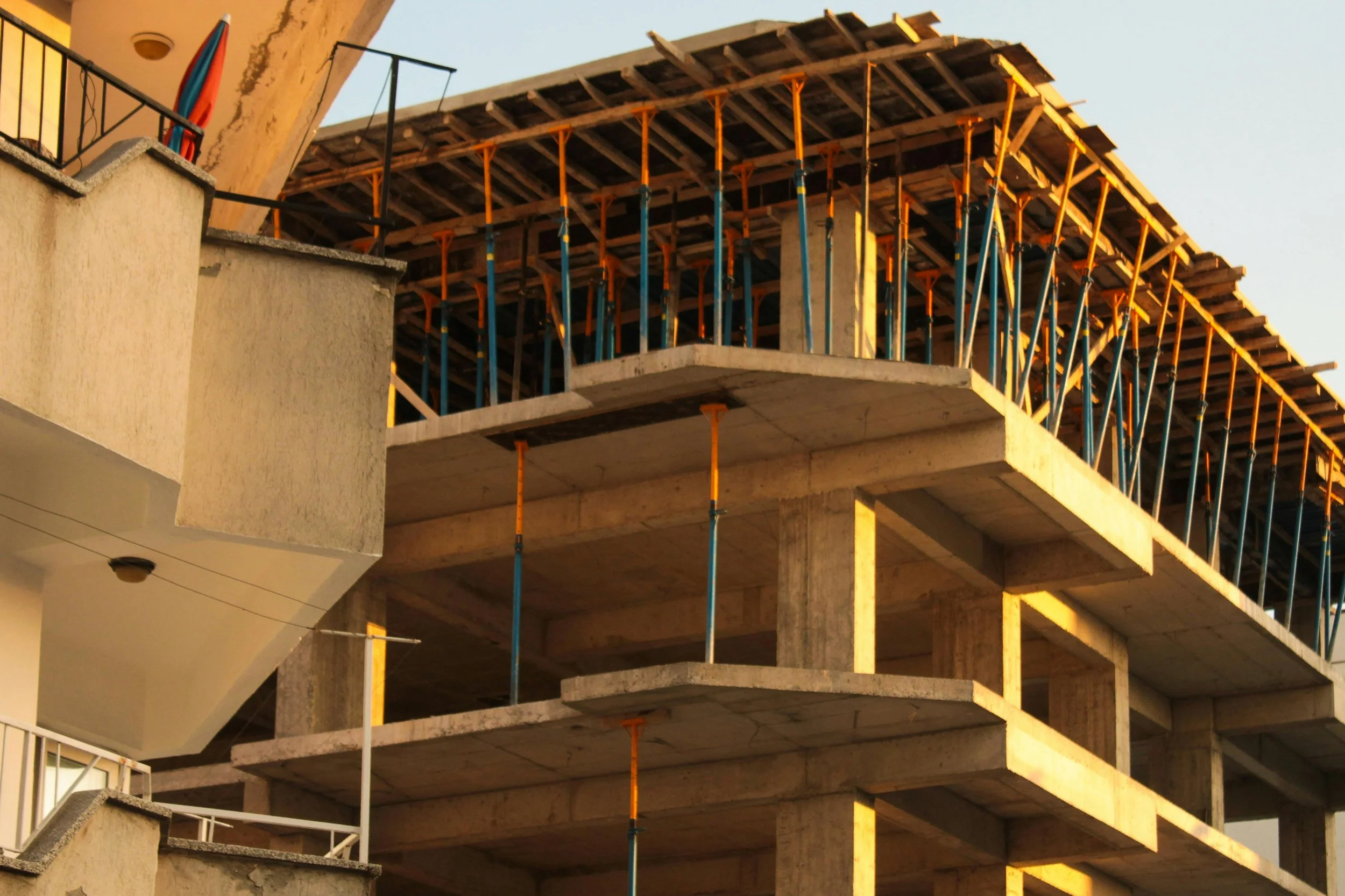 Construction site with multiple floors of a building under construction, showing scaffolding and support beams, with a clear daytime sky in the background.