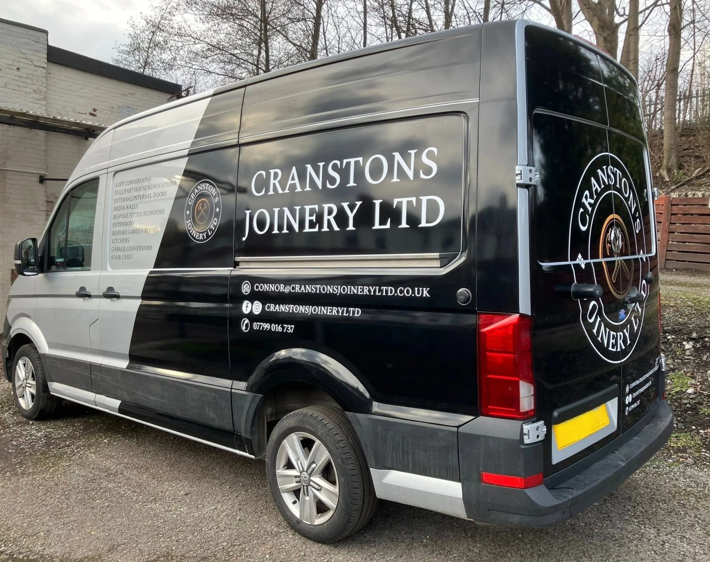 A black company van with advertisements for Cranstons Joinery Ltd on the side and back, parked outdoors near a brick building and trees.